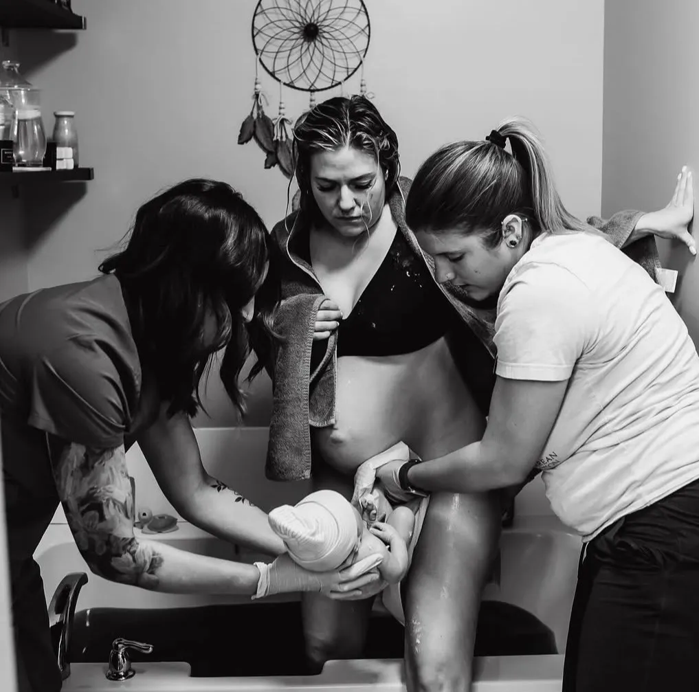 Midwife checking in with a mother at home while her toddler looks on