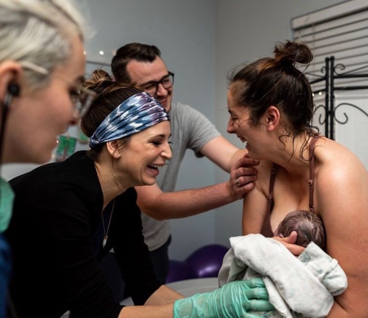 A mother and her partner laughing with the midwives as she holds her newborn moments after a home birth