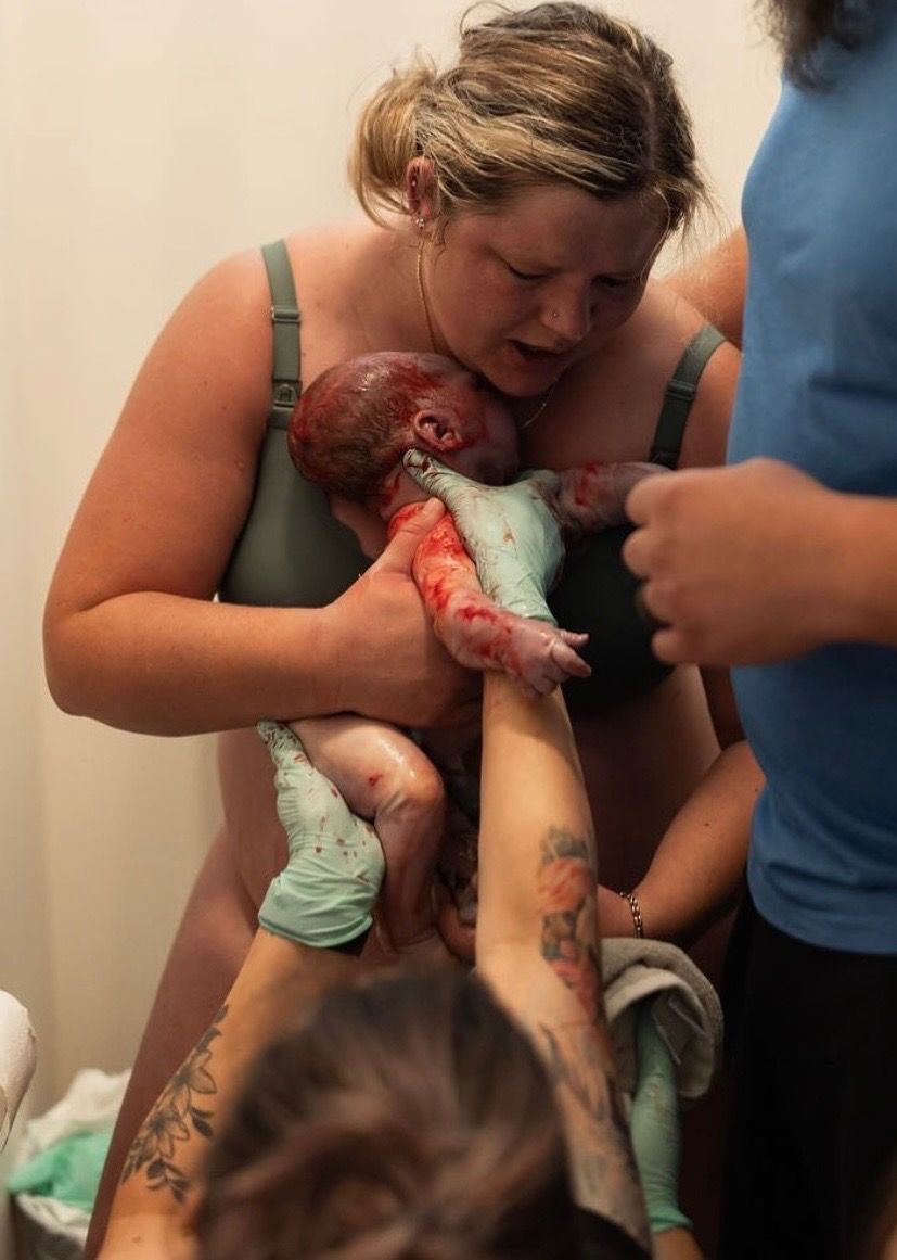 A mother drawing her newborn to her chest after a standing birth, supported by her midwives